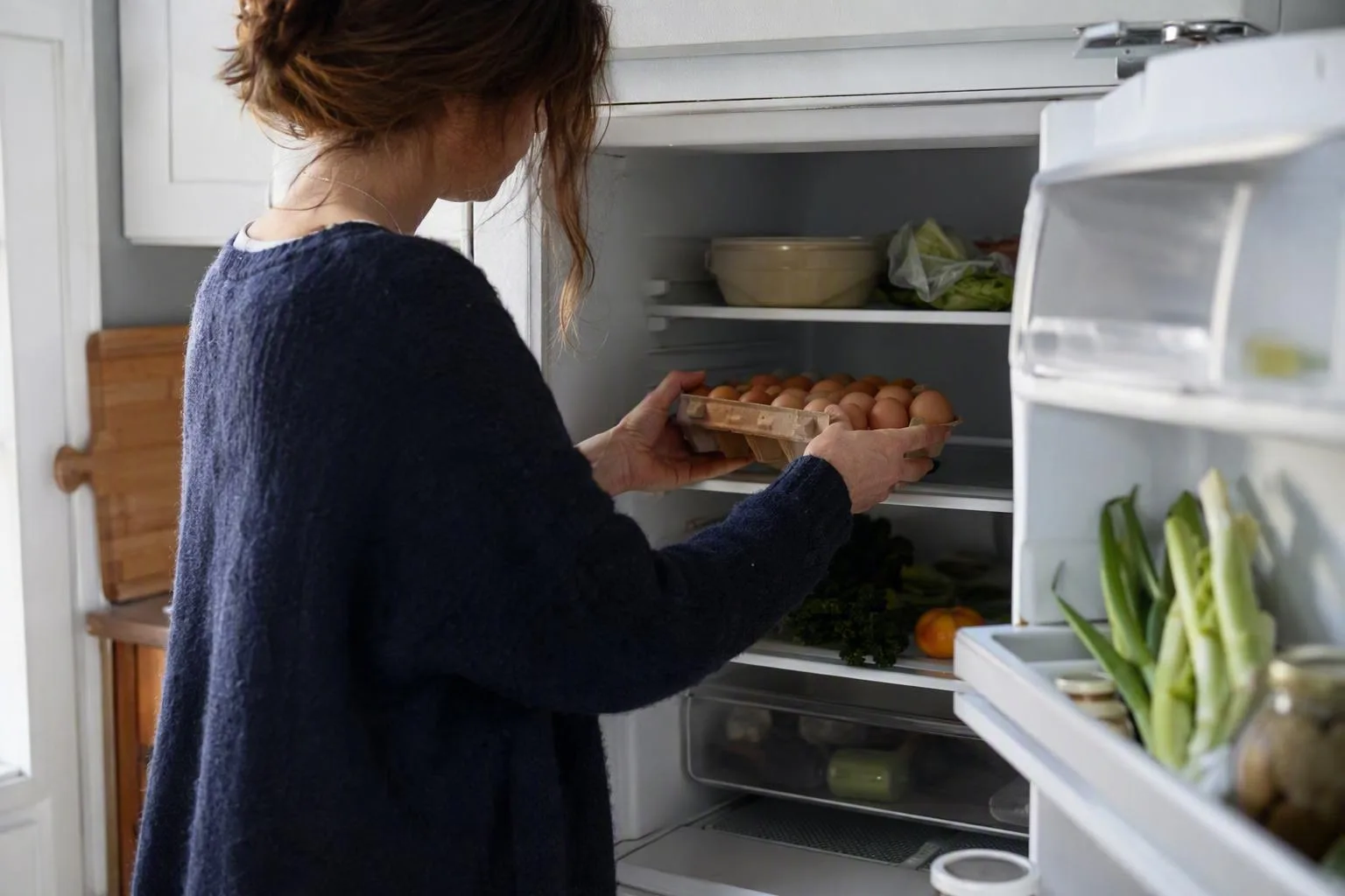 Hands place an unmarked egg carton on an interior refrigerator shelf, away from the door.